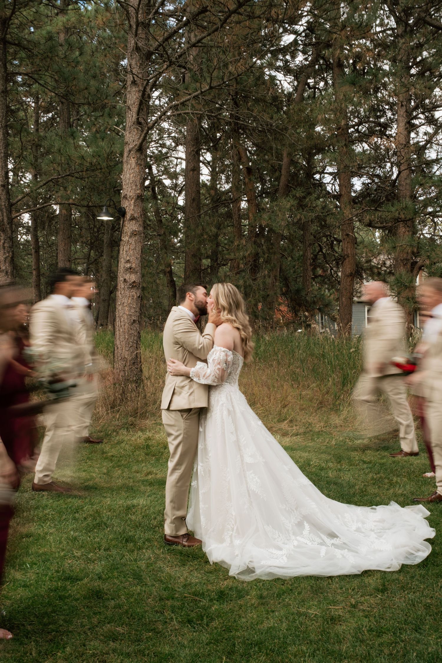 Motion blur captures wedding party dancing and celebrating in a wooded outdoor setting with bride in flowing white gown.