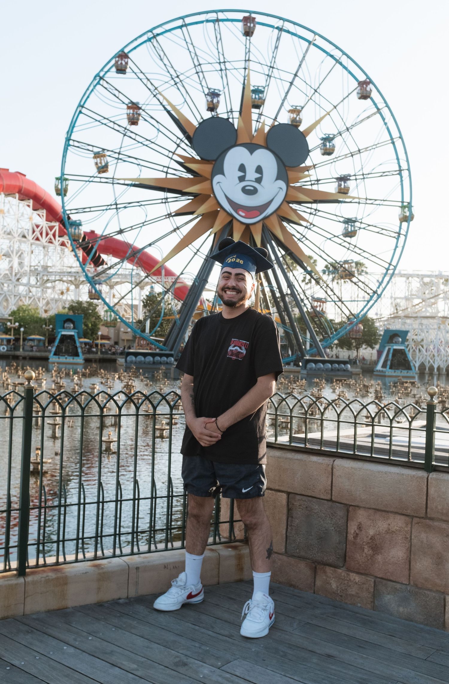 Man smiling in front of Mickey Mouse Ferris wheel at Disney California Adventure park on a sunny day.