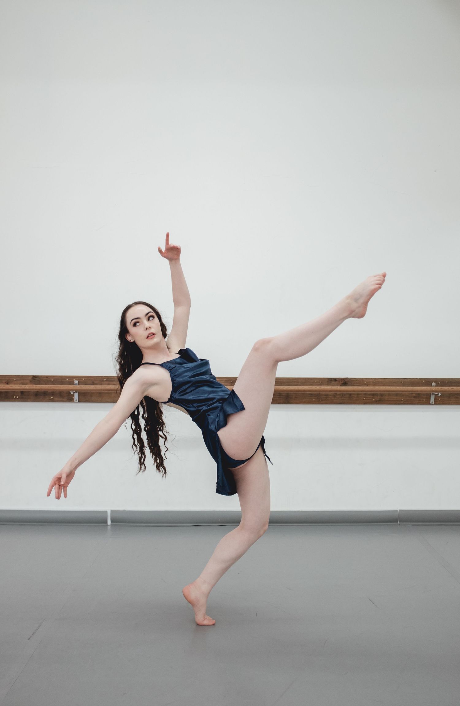 Dancer in navy blue costume performs an elegant pose in a studio with bare feet.