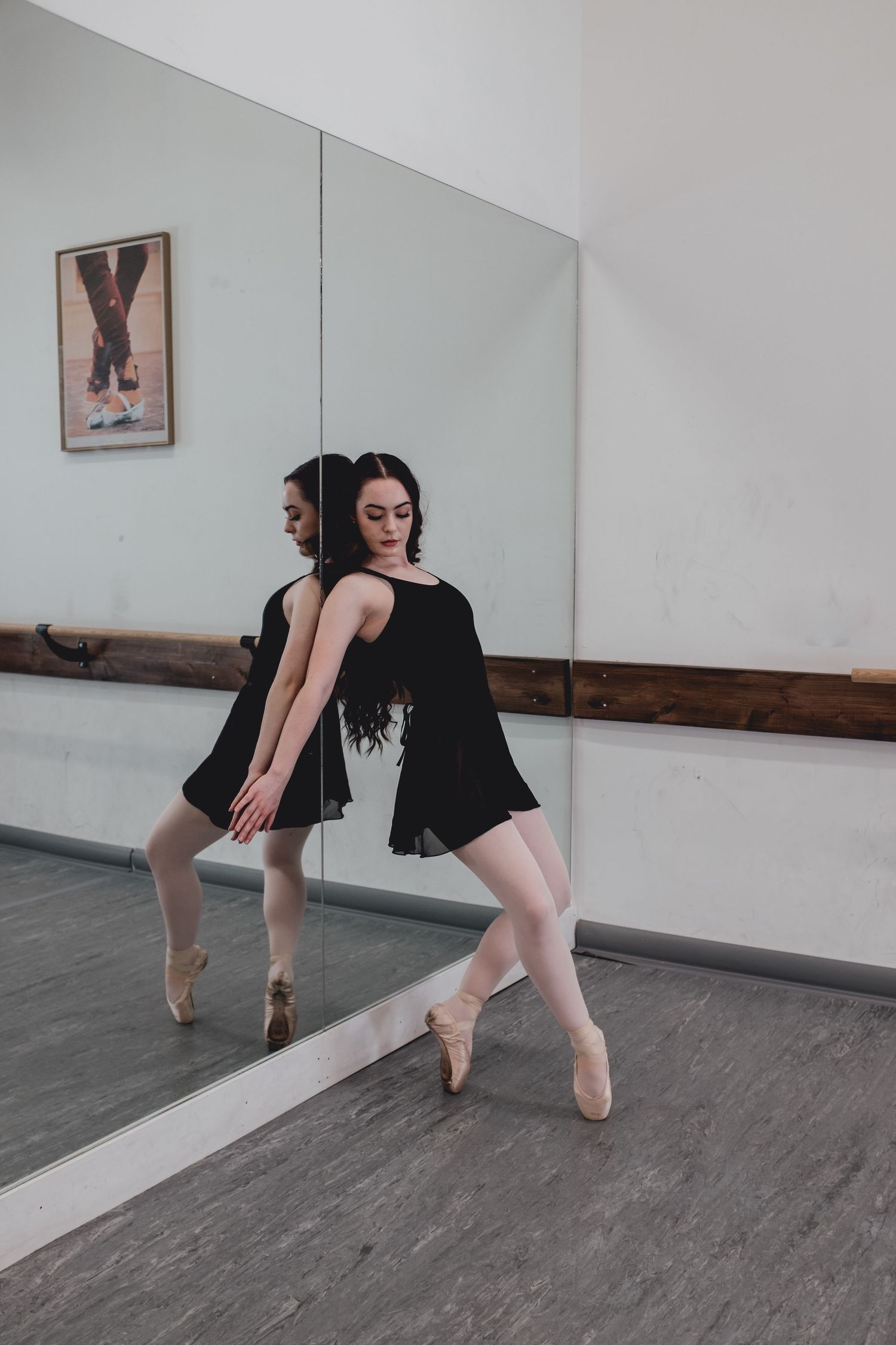 Dancer in black outfit practices ballet moves in front of studio mirror.