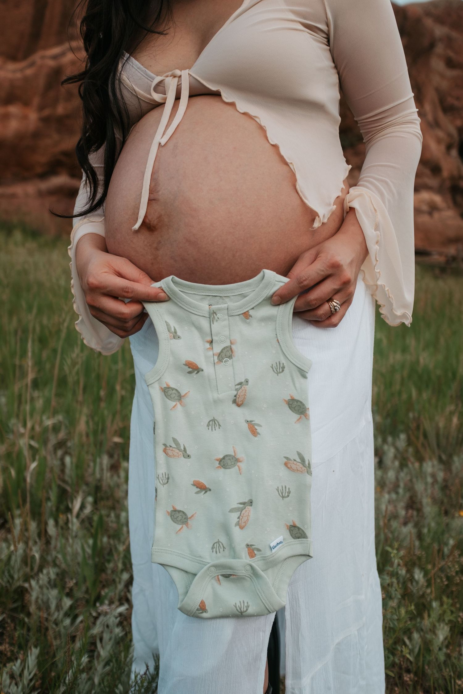 Maternity photo showing a pregnant belly with a mint green baby onesie held against it.