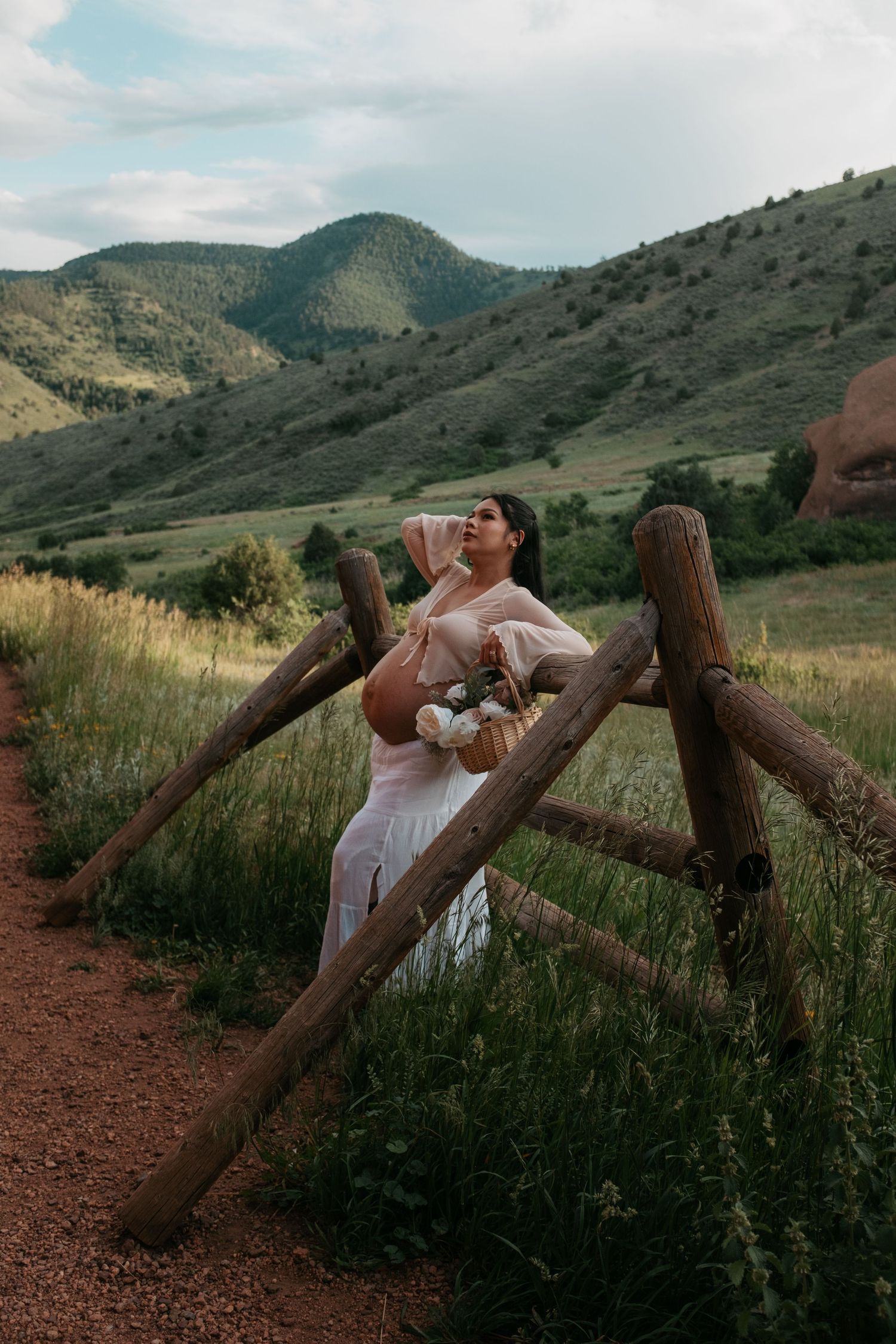 A joyful maternity photo captured by a rustic wooden fence in the Colorado foothills.