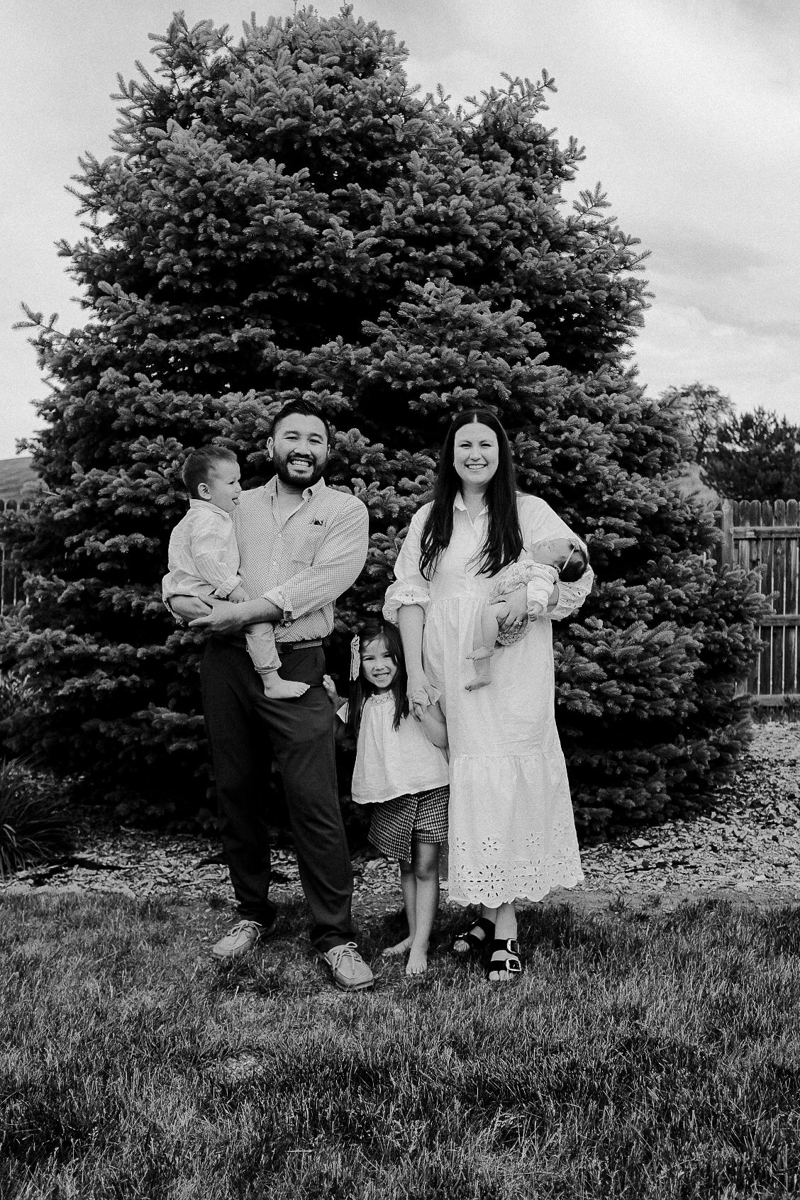 Black and white family portrait in front of a large evergreen tree.