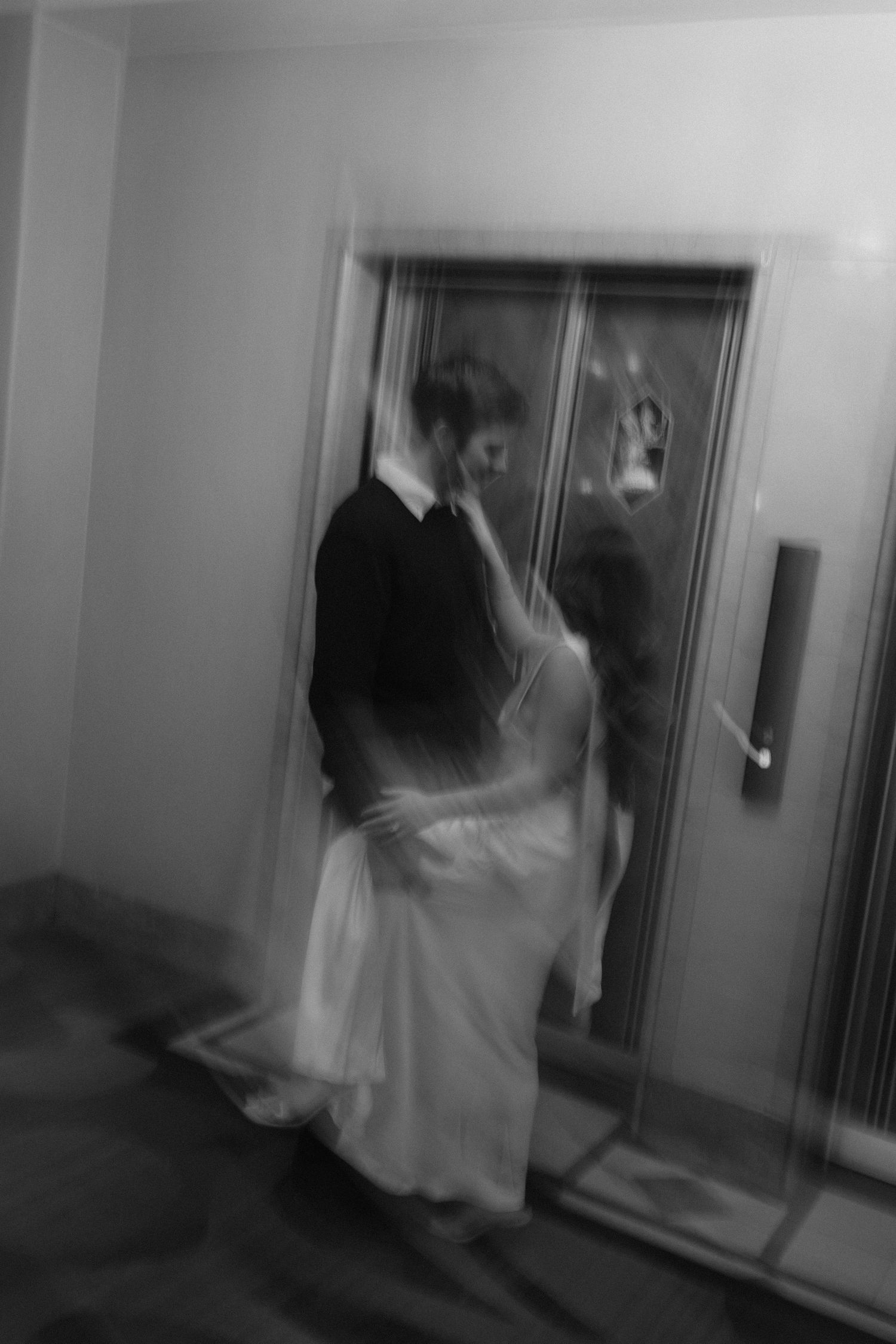 Blurry black and white photo of a bride and groom embracing near elevator doors on their wedding day.