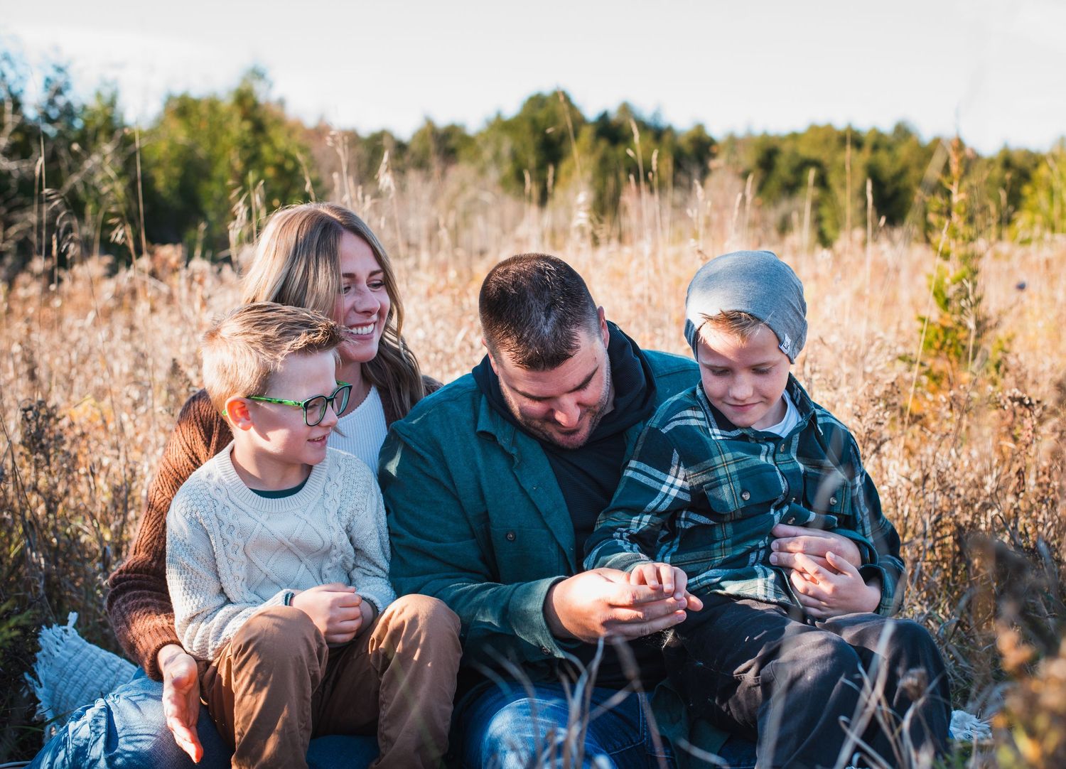 People sitting together in a golden autumn field during golden hour while looking at something together.