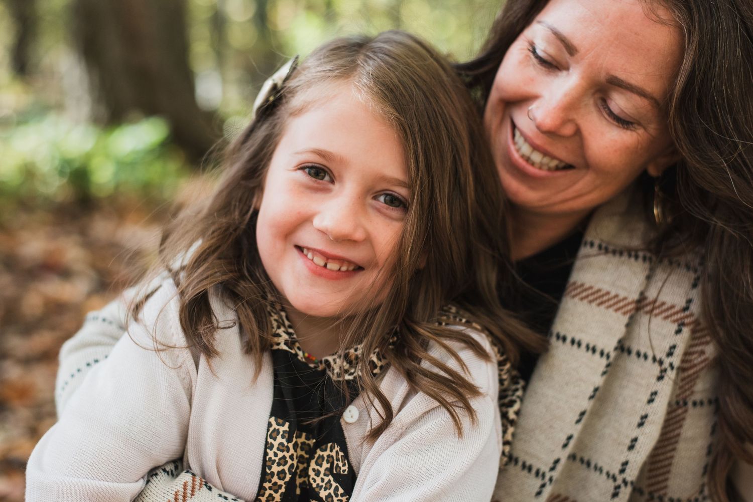 Candid mother and daughter sharing tender moments and laughter together in a natural outdoor forest setting.