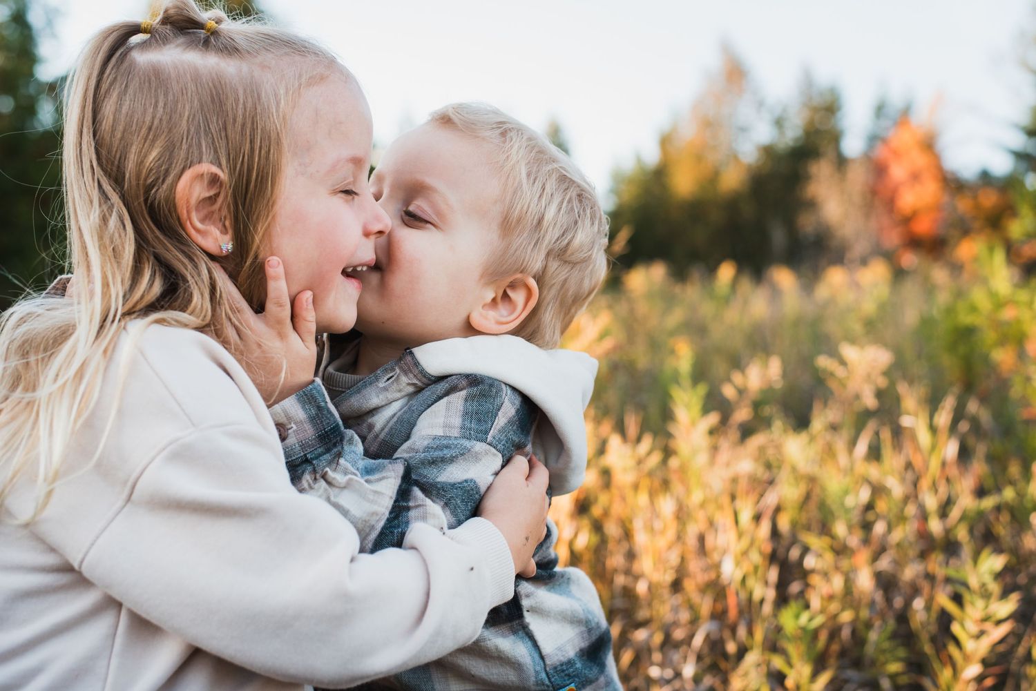 Two children sharing an affectionate moment in a field during autumn.
