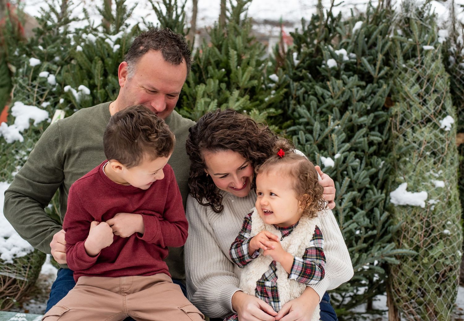 Family members share joyful moments together while picking out a Christmas tree at a seasonal tree farm.