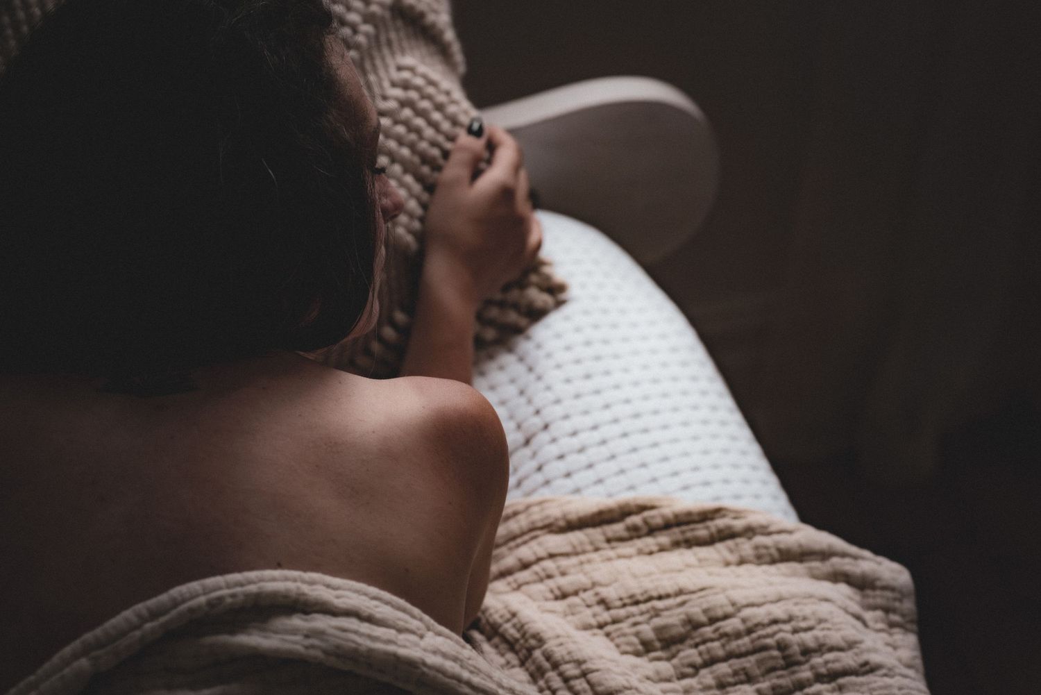 Intimate portrait of someone leaning back in knitted sweater with natural lighting against dark background.