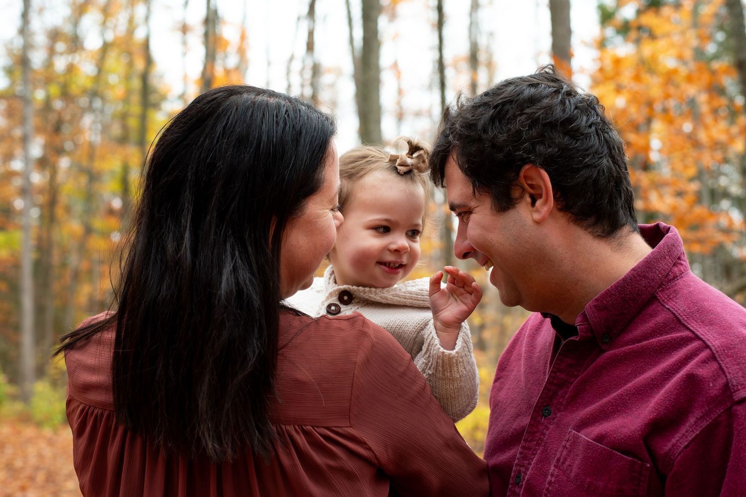 Family of three enjoying autumn forest, parents smiling at happy toddler girl among golden fall foliage.
