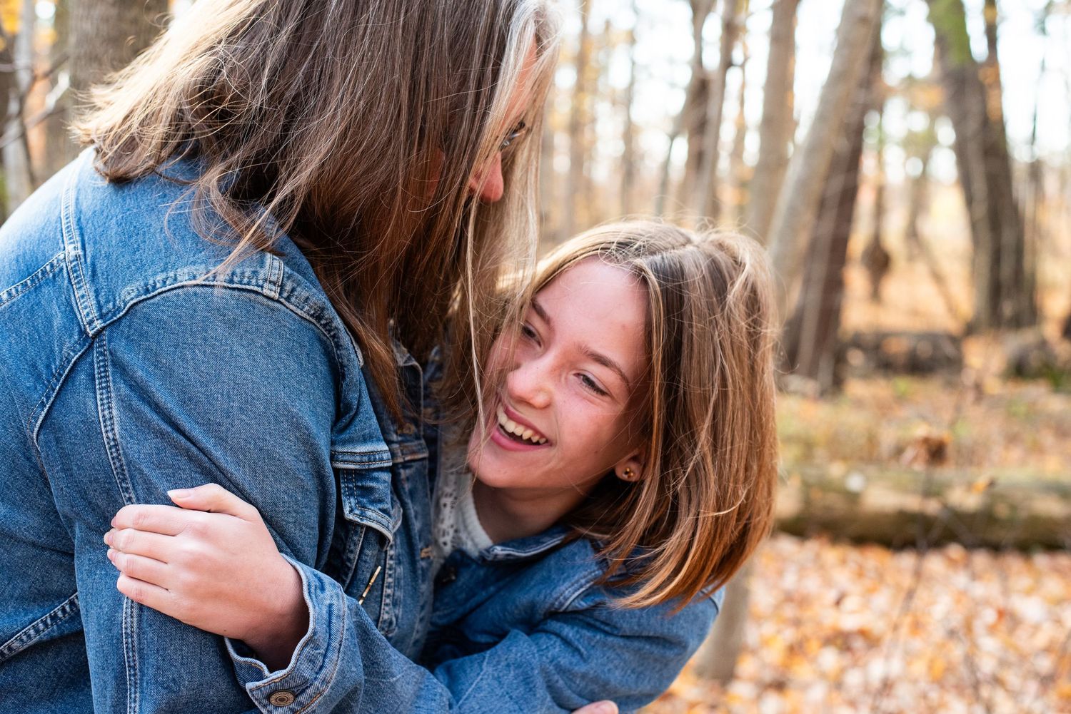 Two people in denim jackets share a joyful embrace in an autumn forest.