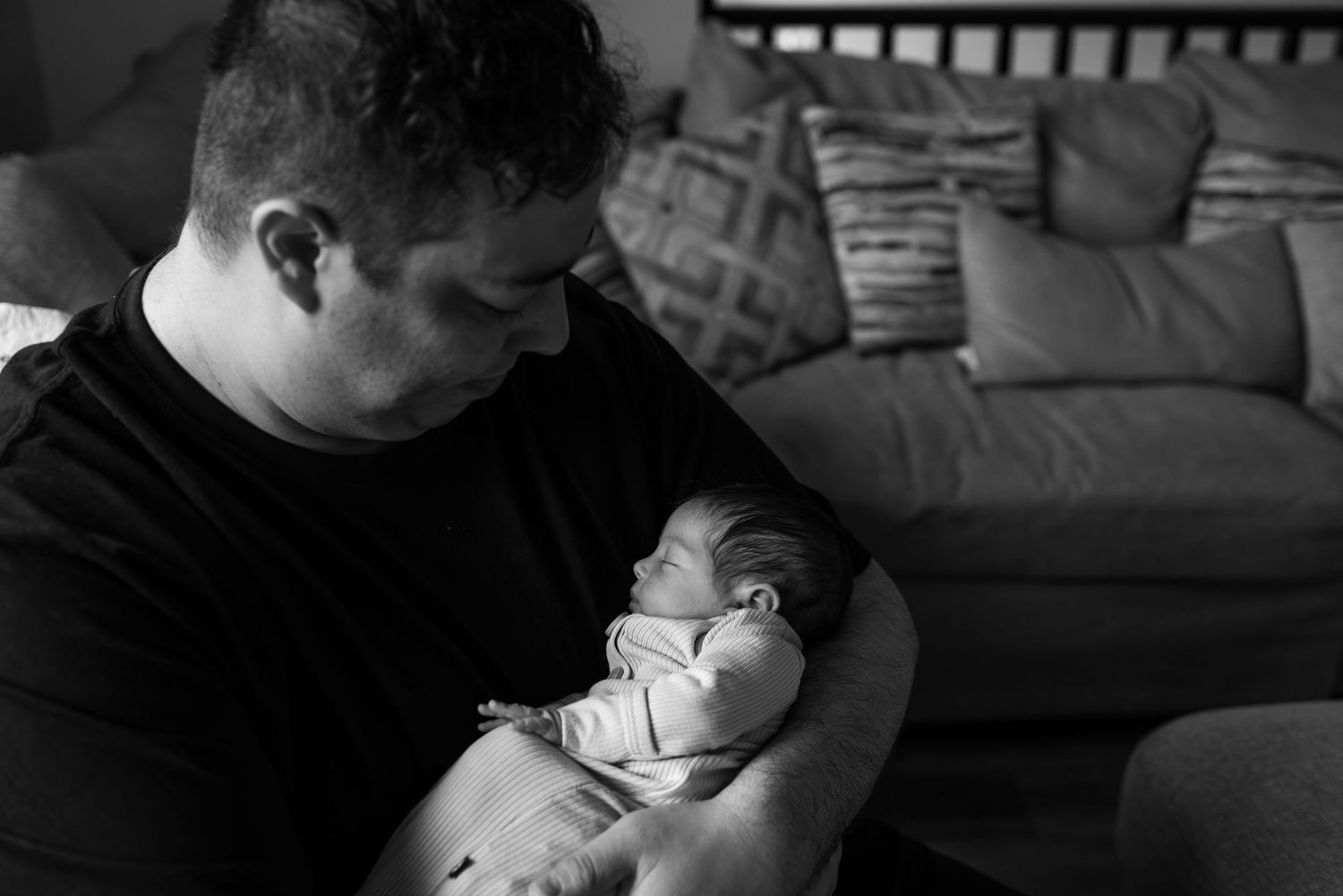 Black and white image of a parent holding a sleeping infant in a living room setting.