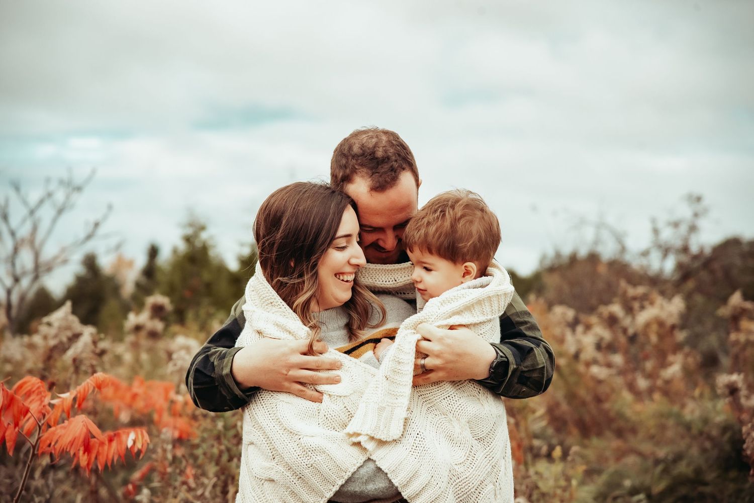 Romantic autumn engagement photo session outdoors with couple embracing in field of dried wild grass.