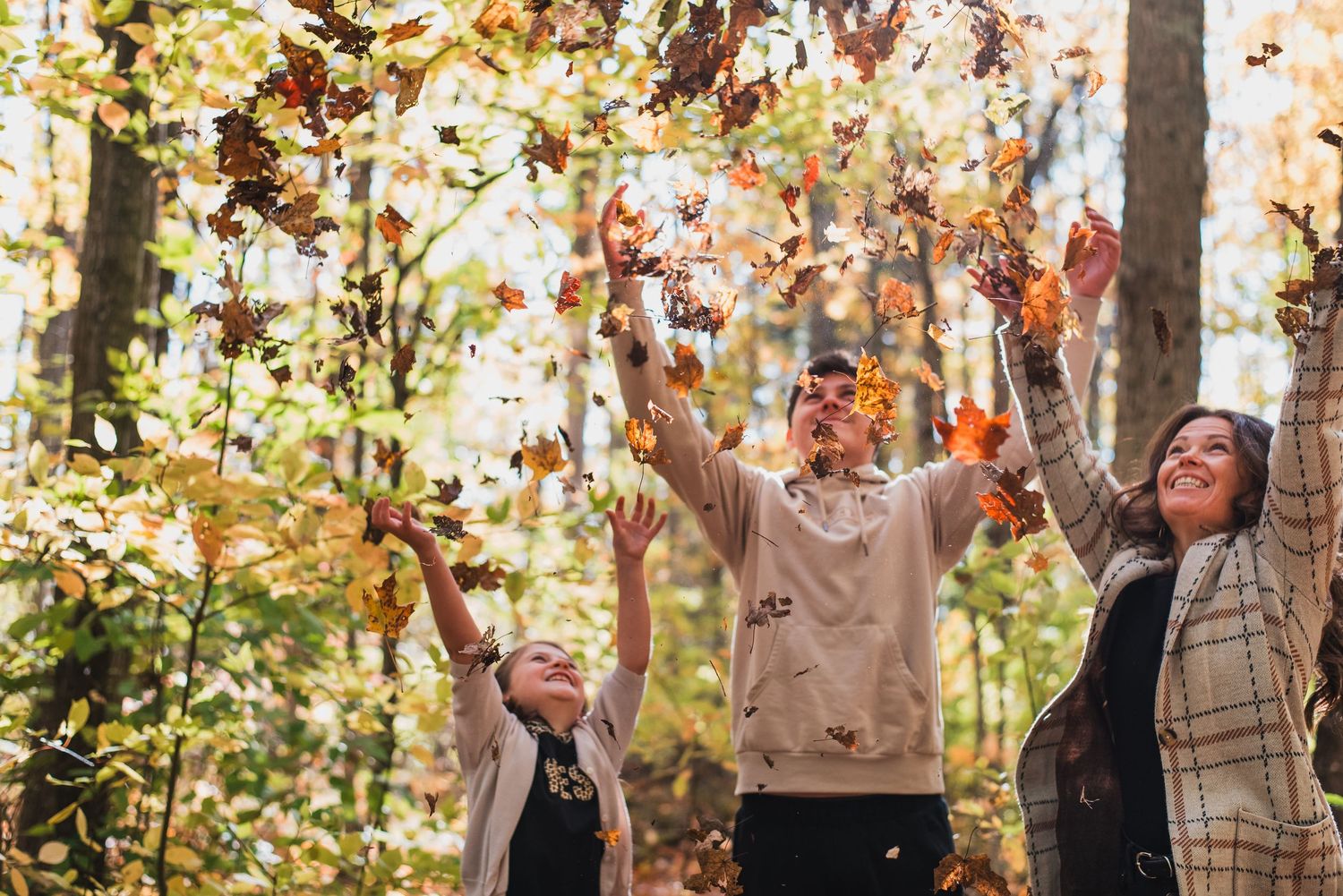 A group of people standing in a forest throwing autumn leaves in the air during a photo session.