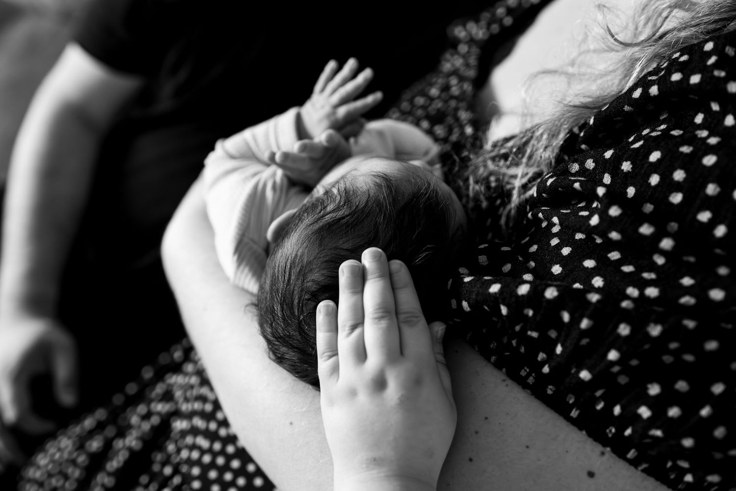 Close up black and white photo of a small baby lying on a polka dot fabric with hands raised.
