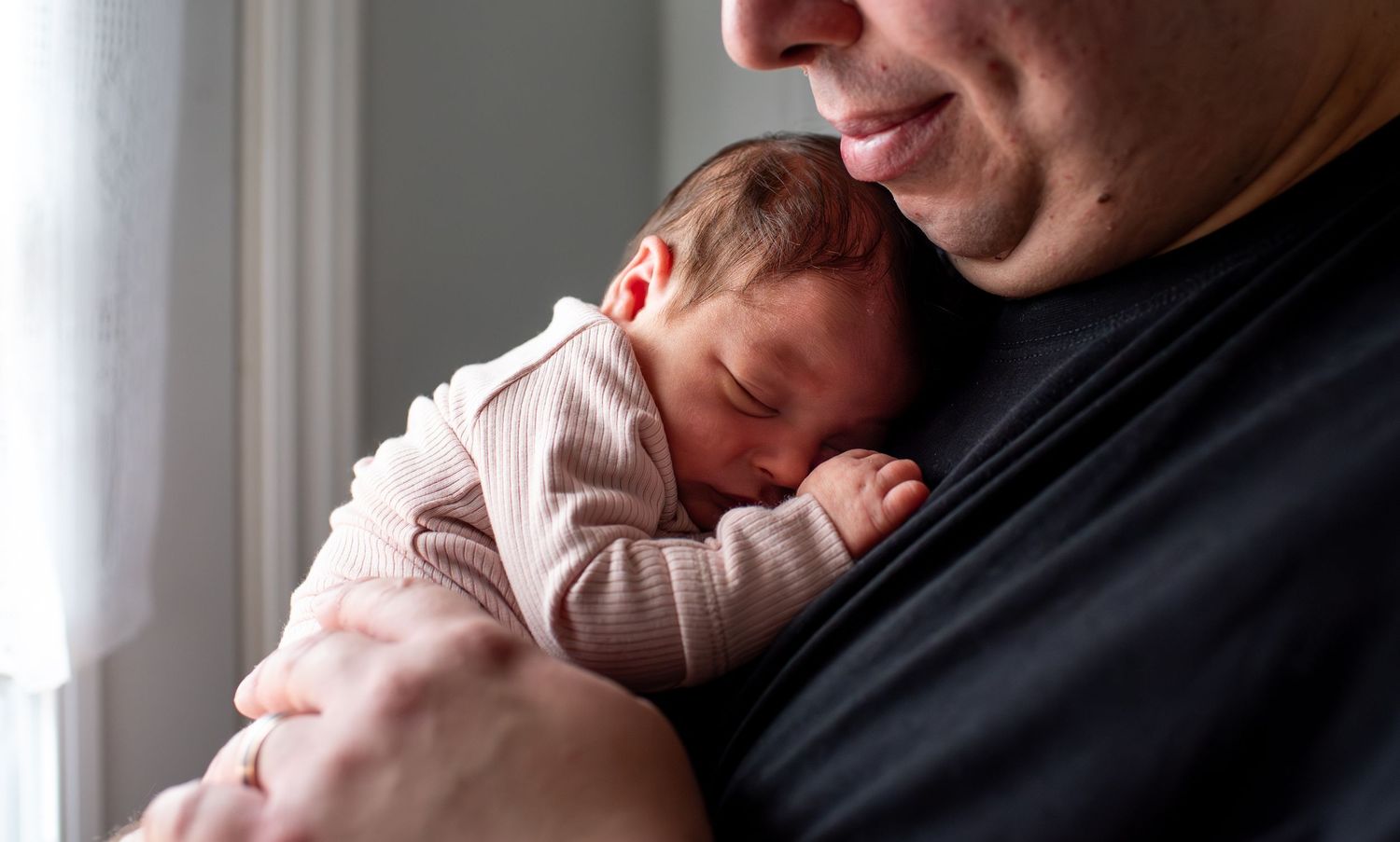 Parent holds sleeping newborn baby against their chest in tender nurturing moment.