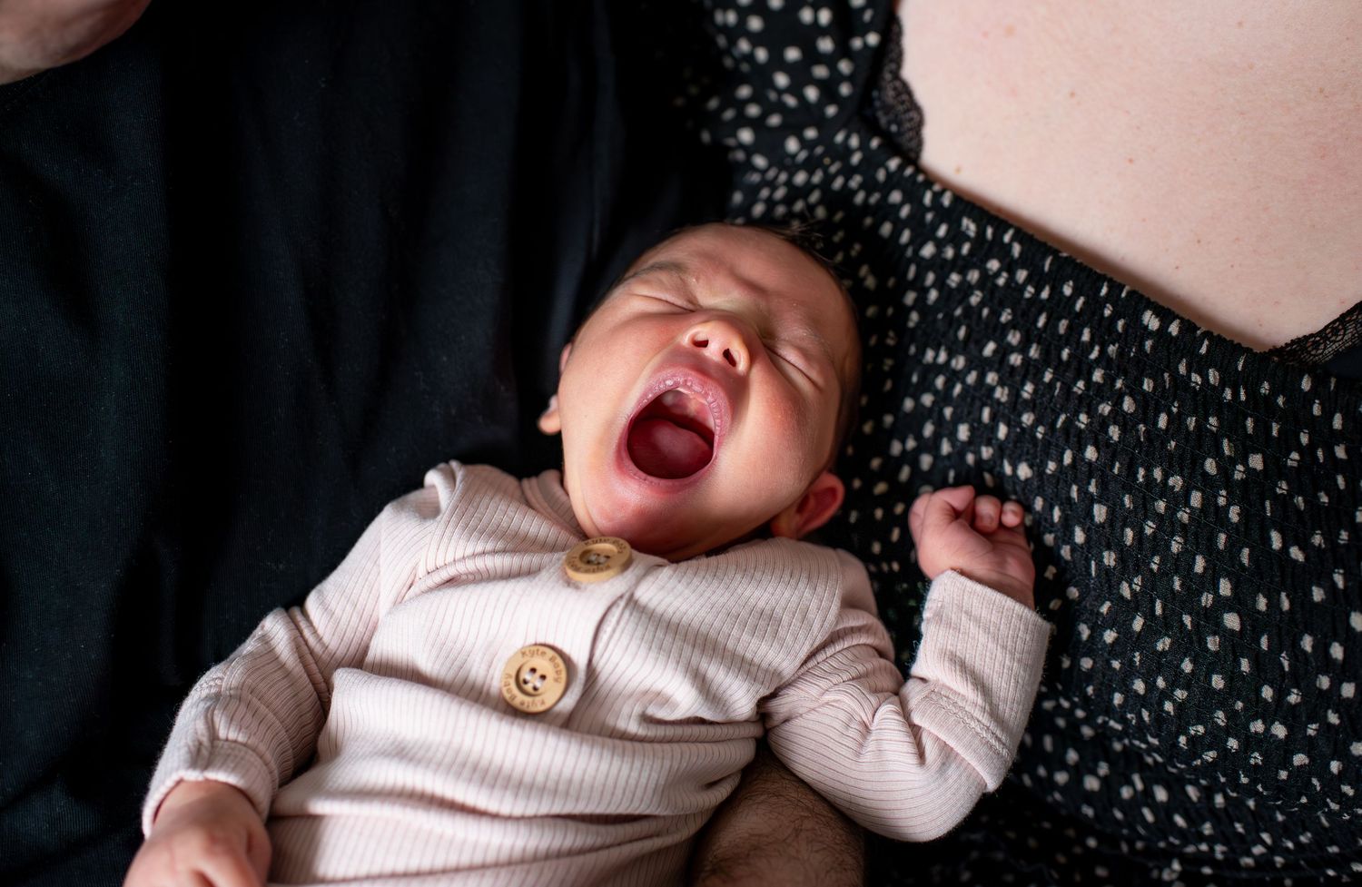 A sleeping baby lies on a polka dot surface in a soft pink onesie, shown at different angles and expressions.