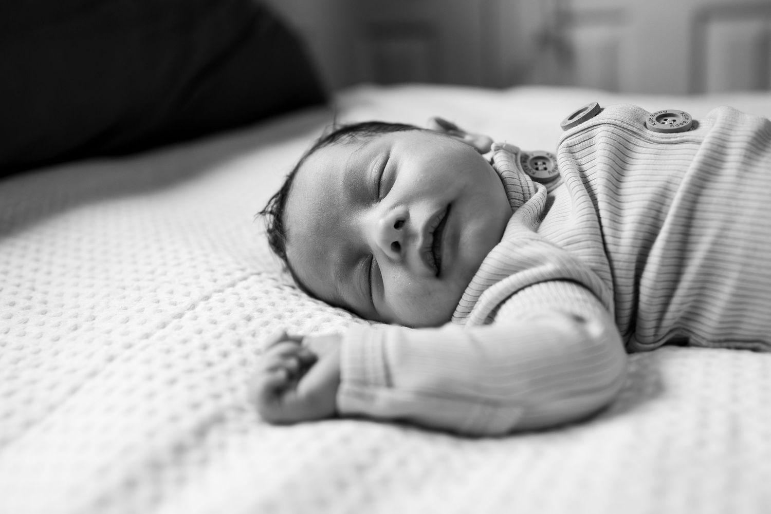A sleeping newborn baby in black and white, wearing a striped onesie while resting peacefully on white bedding.