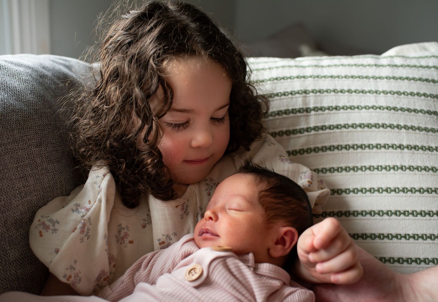 Siblings sharing a tender moment on striped pillow as older child watches over sleeping infant.