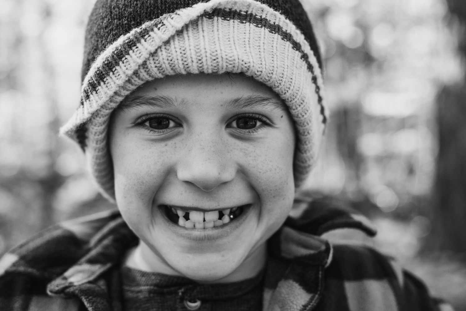 Closeup black and white portrait of child wearing winter hat and camouflage coat smiling at camera.
