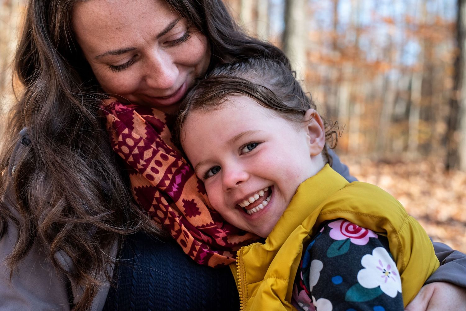 A parent and young child share joyful affectionate moments together while playing outdoors in an autumn forest setting.