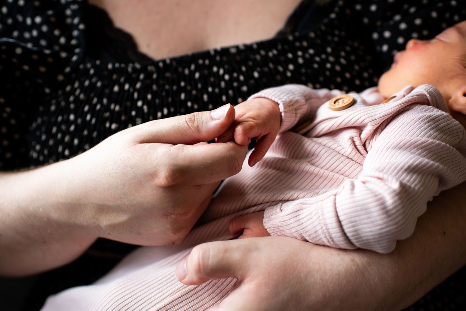 An infant lying on polka dot fabric reaches towards a hand extending from the side of the frame.