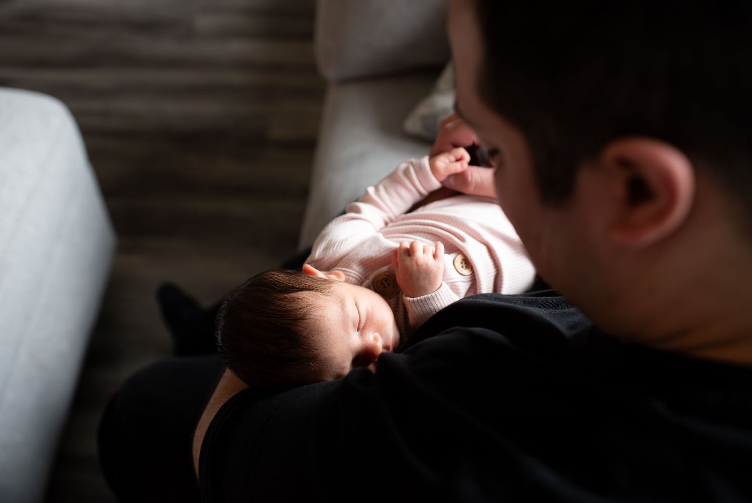 A small baby rests peacefully on someone's lap while being cradled in a dimly lit room.