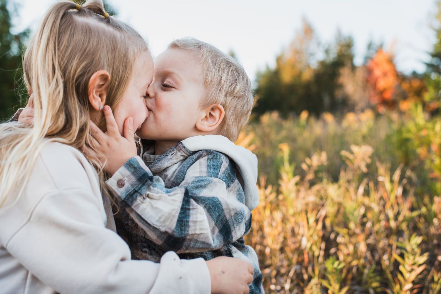 A tender autumn outdoor portrait shows affectionate moments shared in a field with golden sunlight and fall foliage.