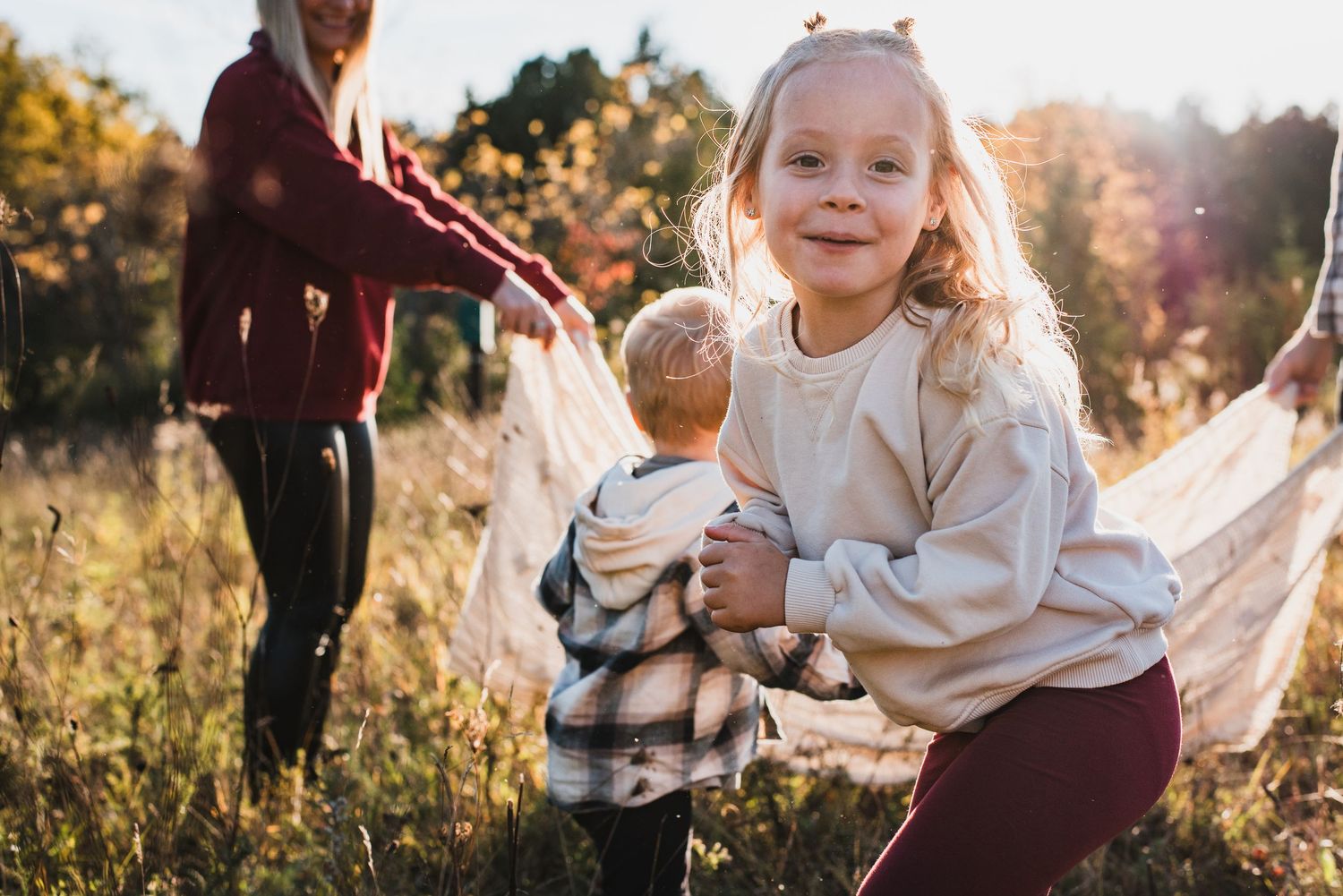 Child in white top plays with toy doll in sunny autumn meadow as sun flares through golden grass.