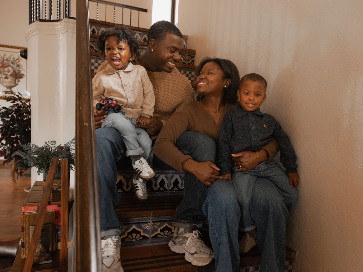 Happy African American family of four laughing together on decorated indoor staircase steps.