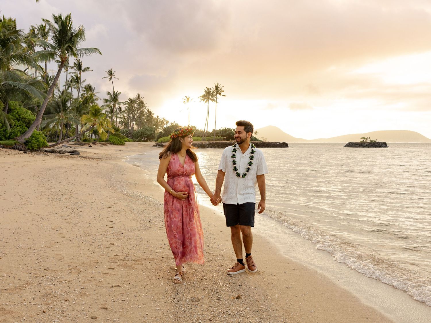 Couple holding hands walking on tropical beach at sunset with palm trees and ocean waves.