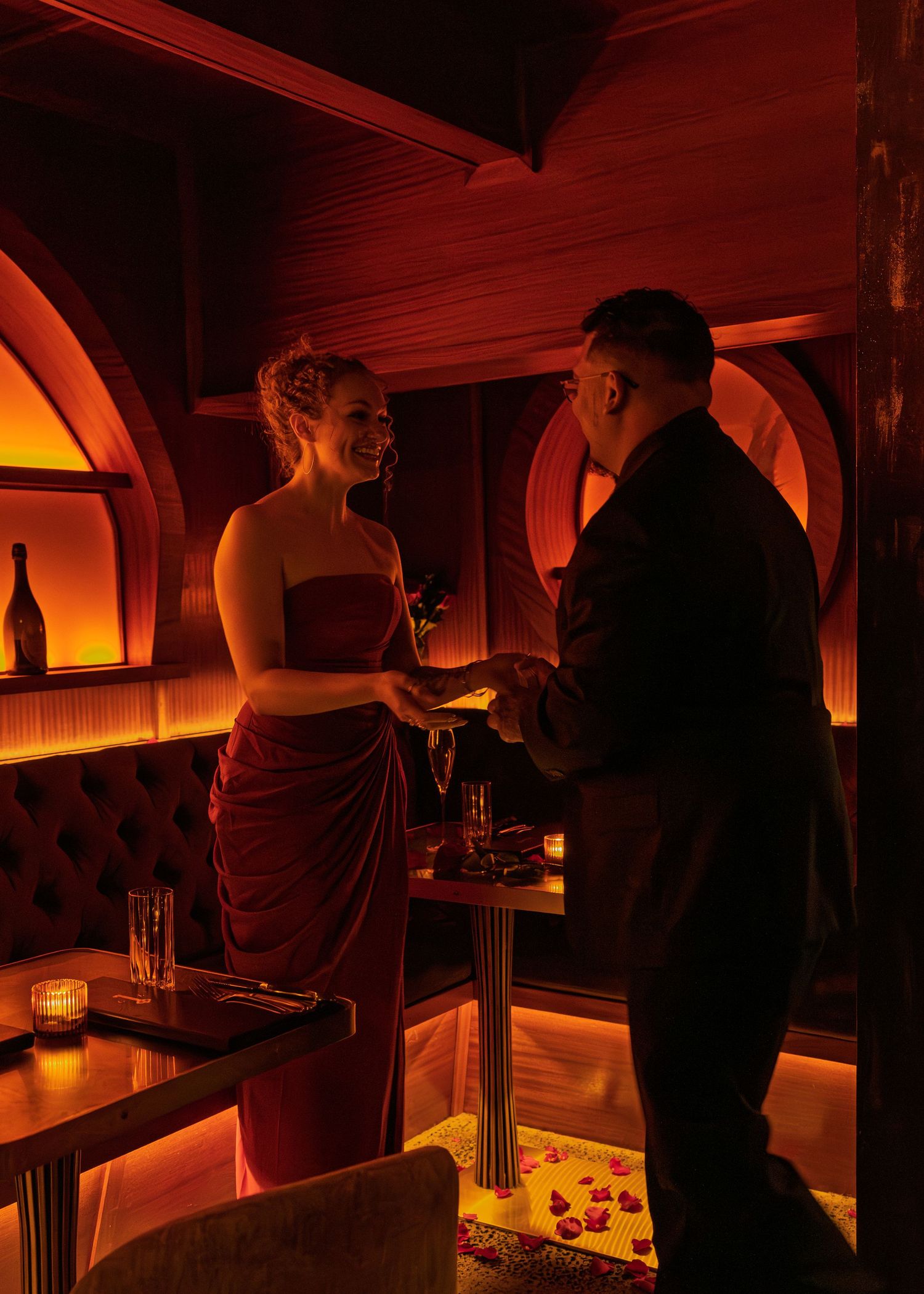 Couple sharing a romantic moment in a dimly lit bar with warm red ambient lighting and arched decor.