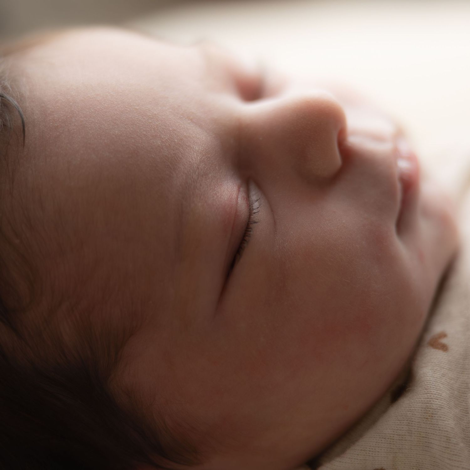 Close-up of a peaceful sleeping newborn baby with soft skin and dark hair in warm, gentle lighting.
