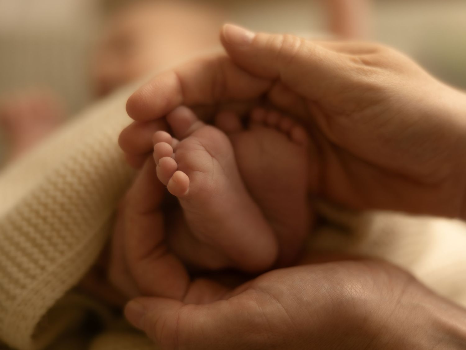 Adult hands gently cradling tiny newborn baby feet, wrapped in a soft blanket, symbolizing love and new life.