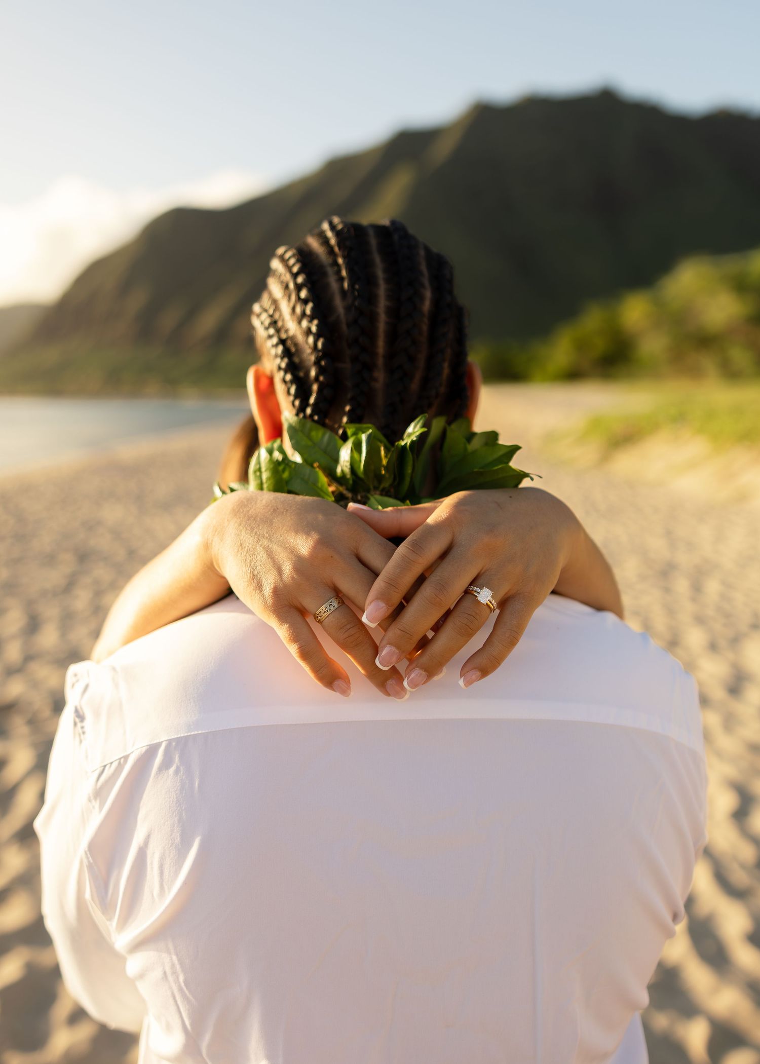 Close-up of bride and groom on sandy Hawaiian beach, showing wedding rings and tropical lei.