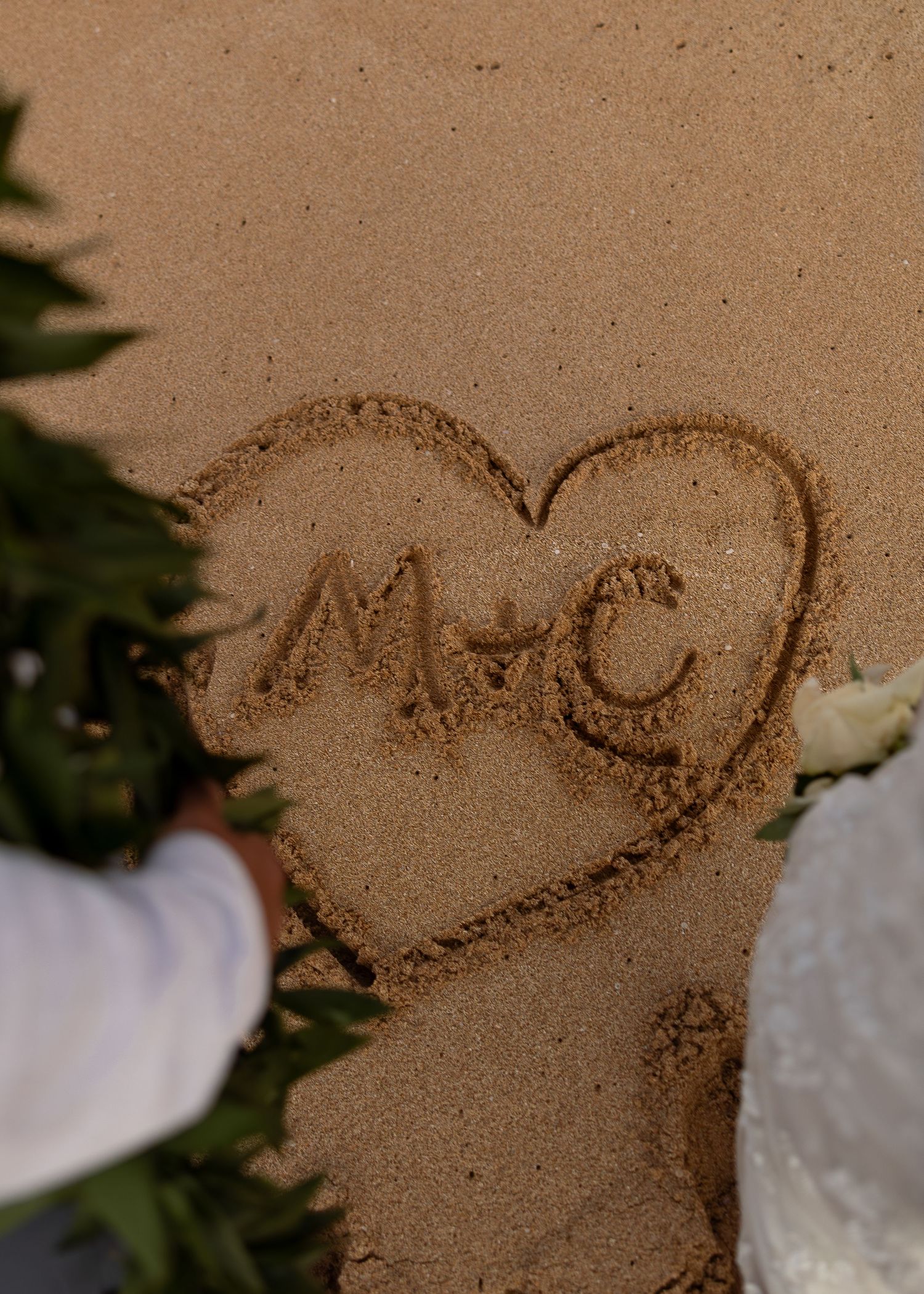 Heart drawn in sand with initials M and C at a beach wedding ceremony.