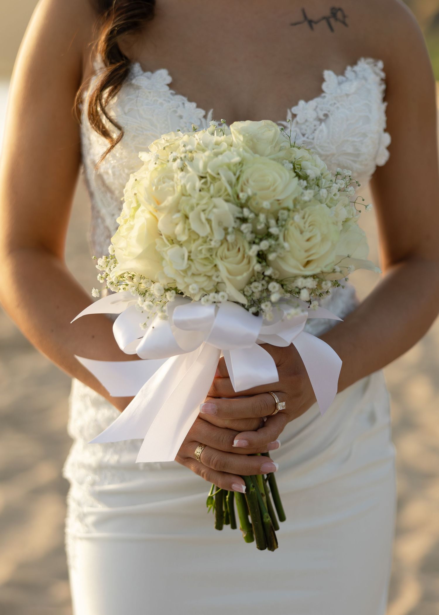 Bride in white lace dress holding elegant bouquet of white roses and baby's breath tied with satin ribbon.