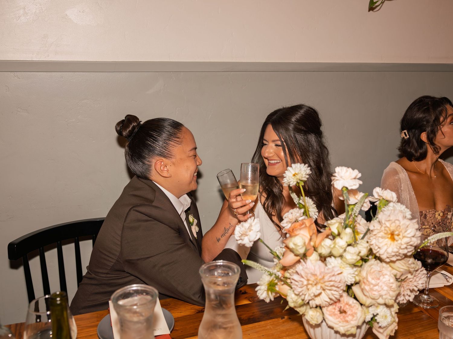 A couple in wedding attire toasting with champagne glasses at a floral-decorated reception table.