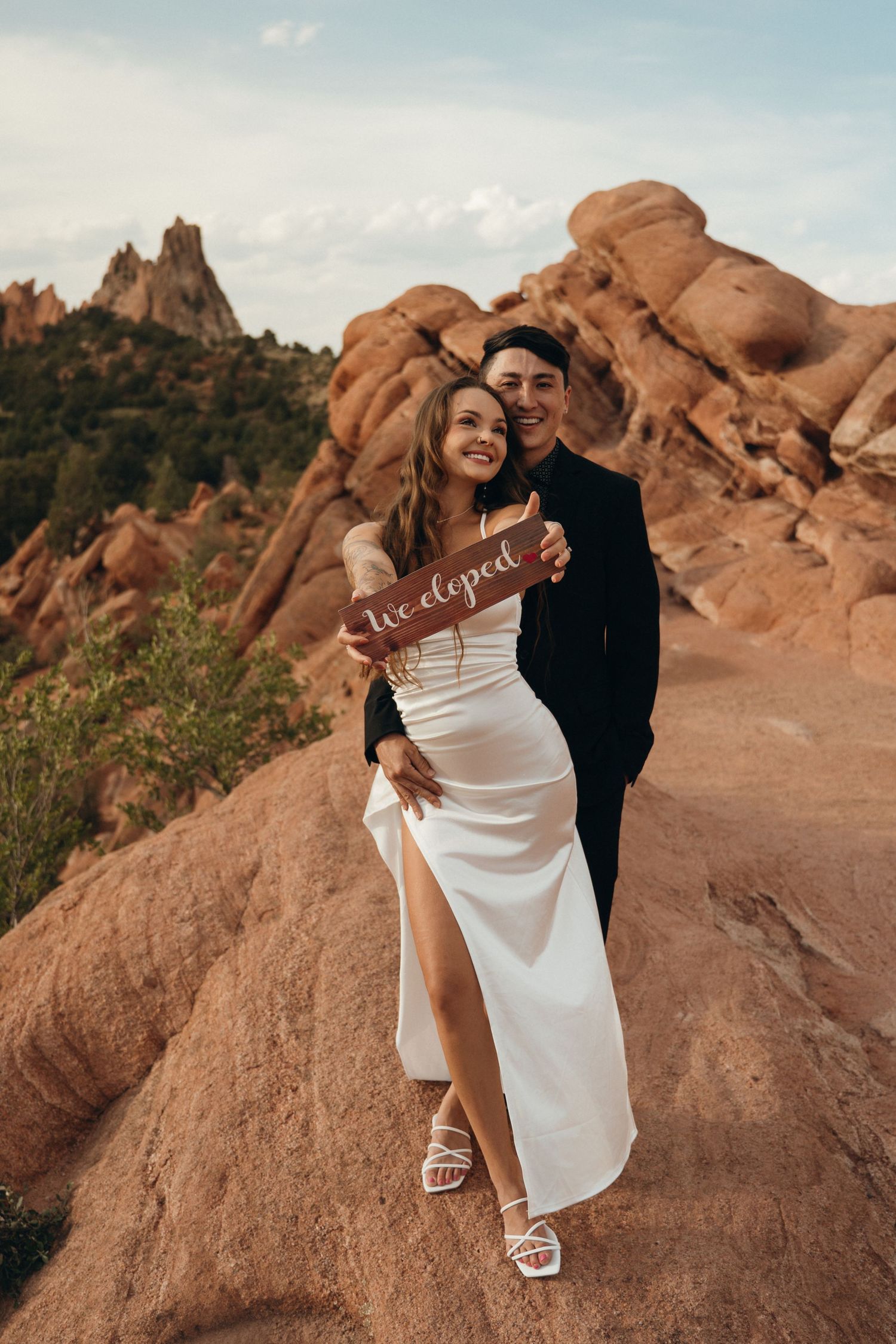 A couple poses for a wedding photo at sunset among striking red rock formations in a desert landscape.