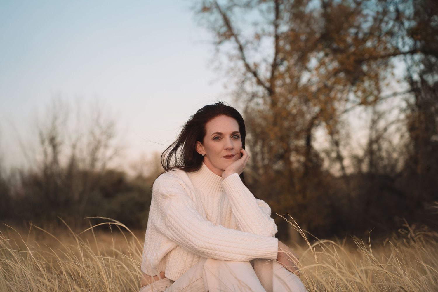 Person in soft pink sweater sitting in tall grass during sunset.