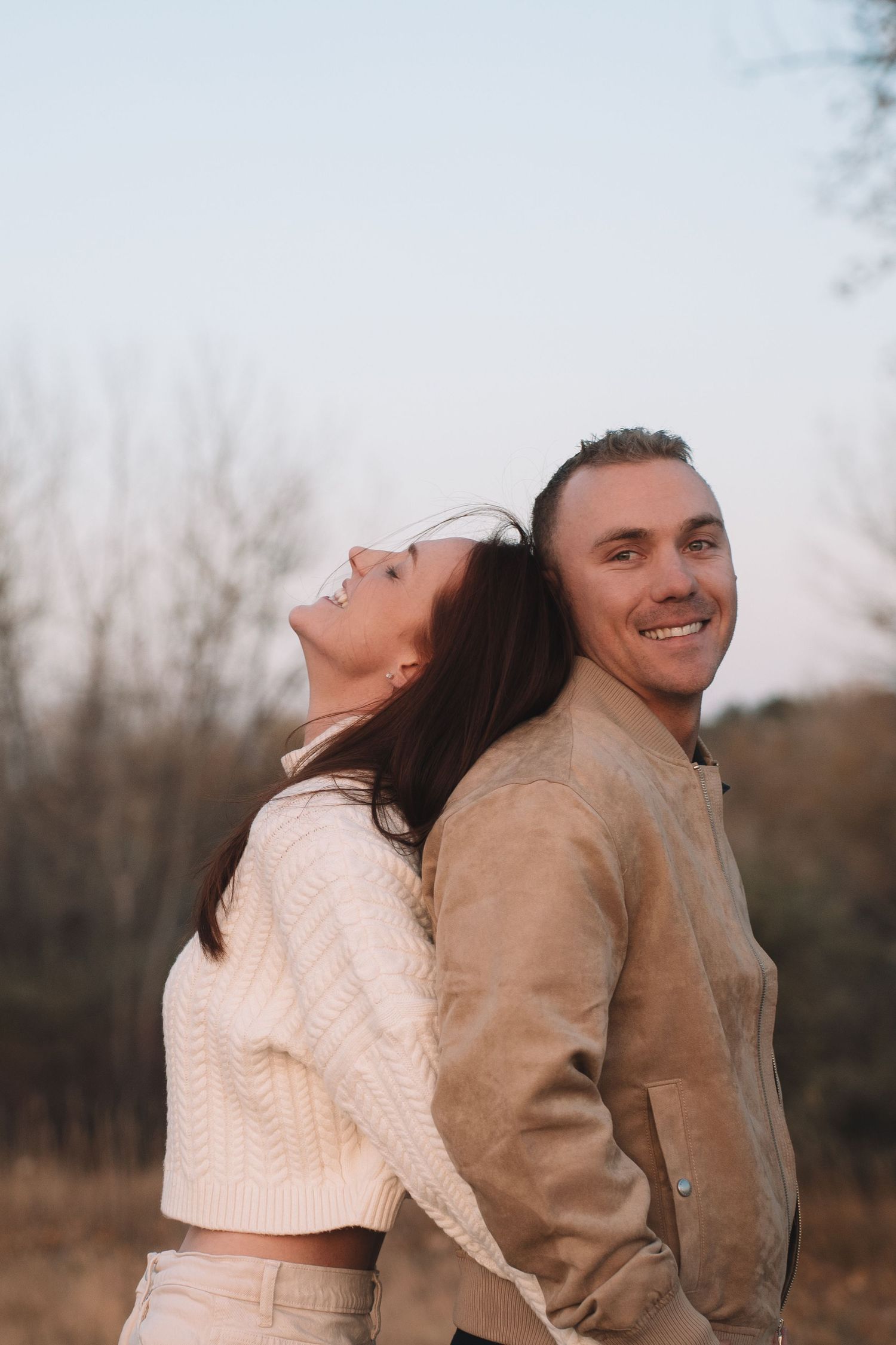 A couple wearing light colored clothing shares a playful moment in a rustic outdoor setting.
