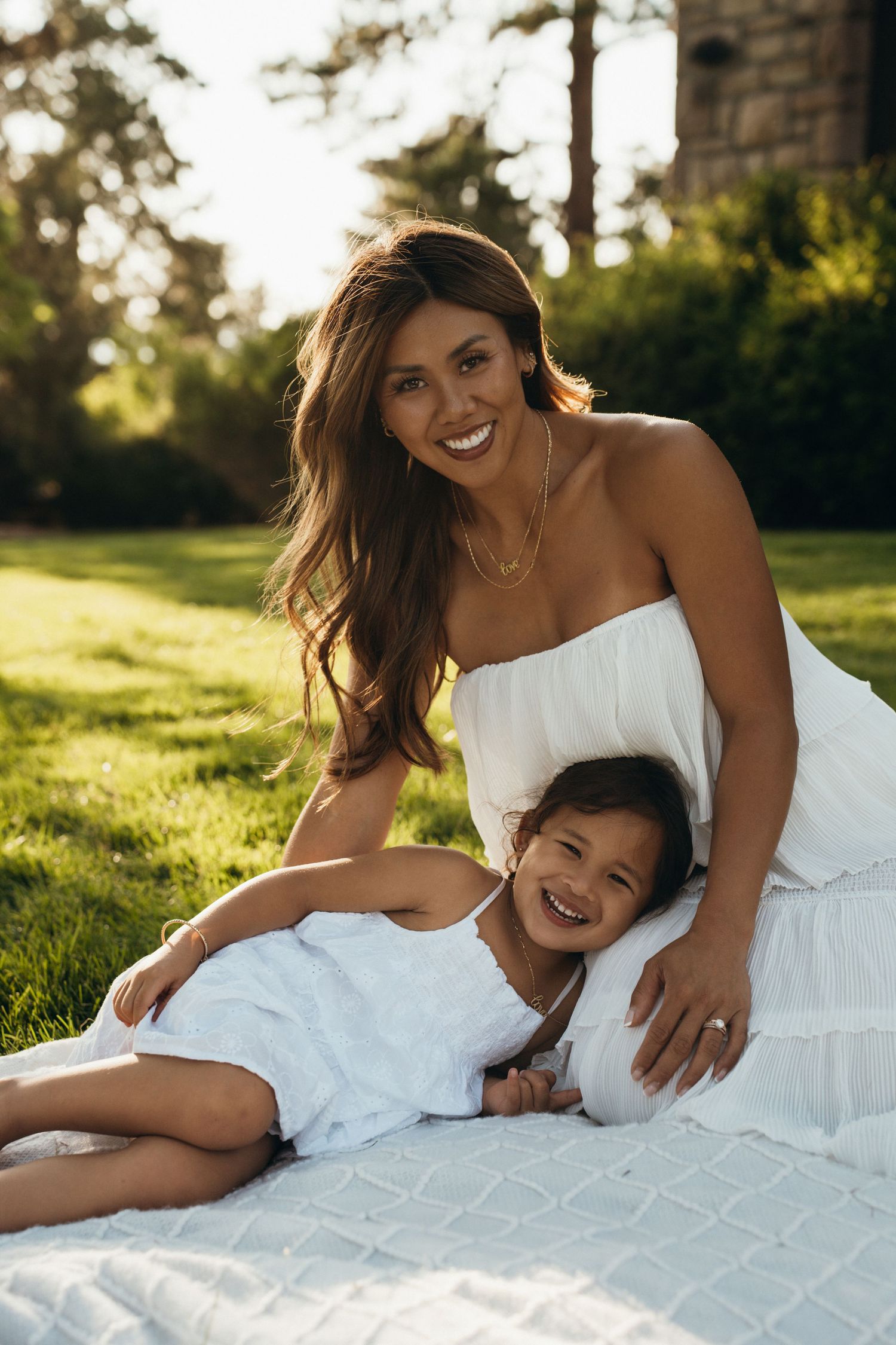 Mother and child in white dress laying on grass during golden hour sunset in a series of candid portrait photos.