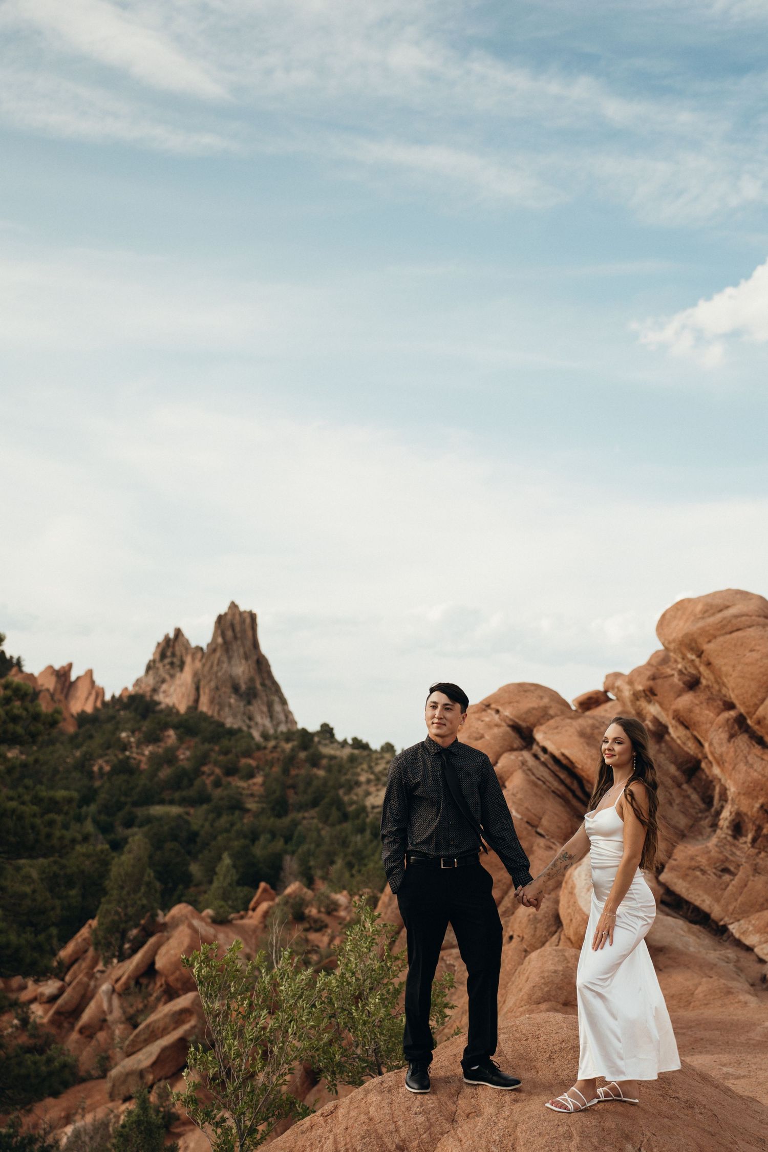 A couple shares an intimate moment against stunning red rock formations in a desert landscape at sunset.