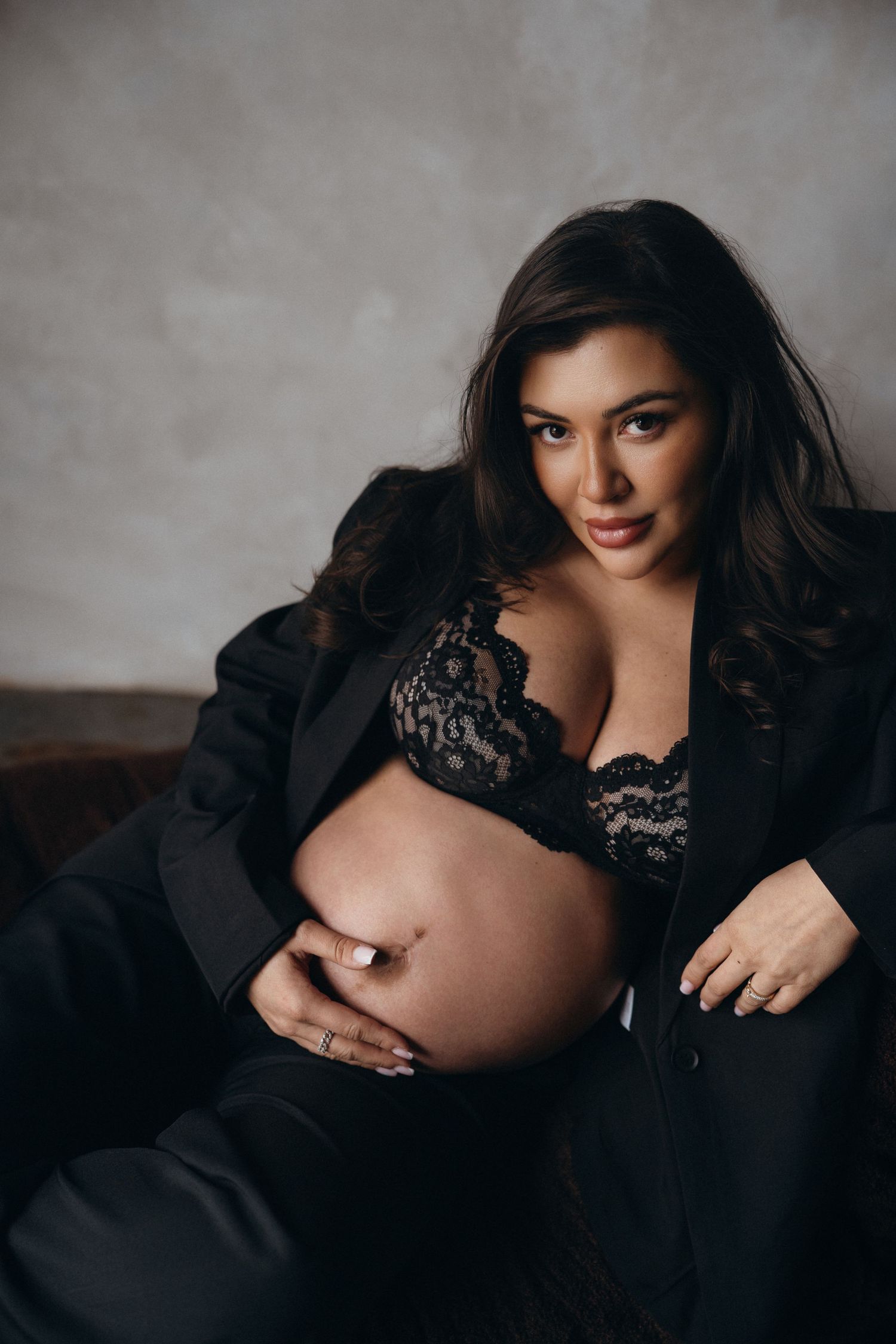 A maternity photo series showing an expectant mother in black lace against a gray backdrop.