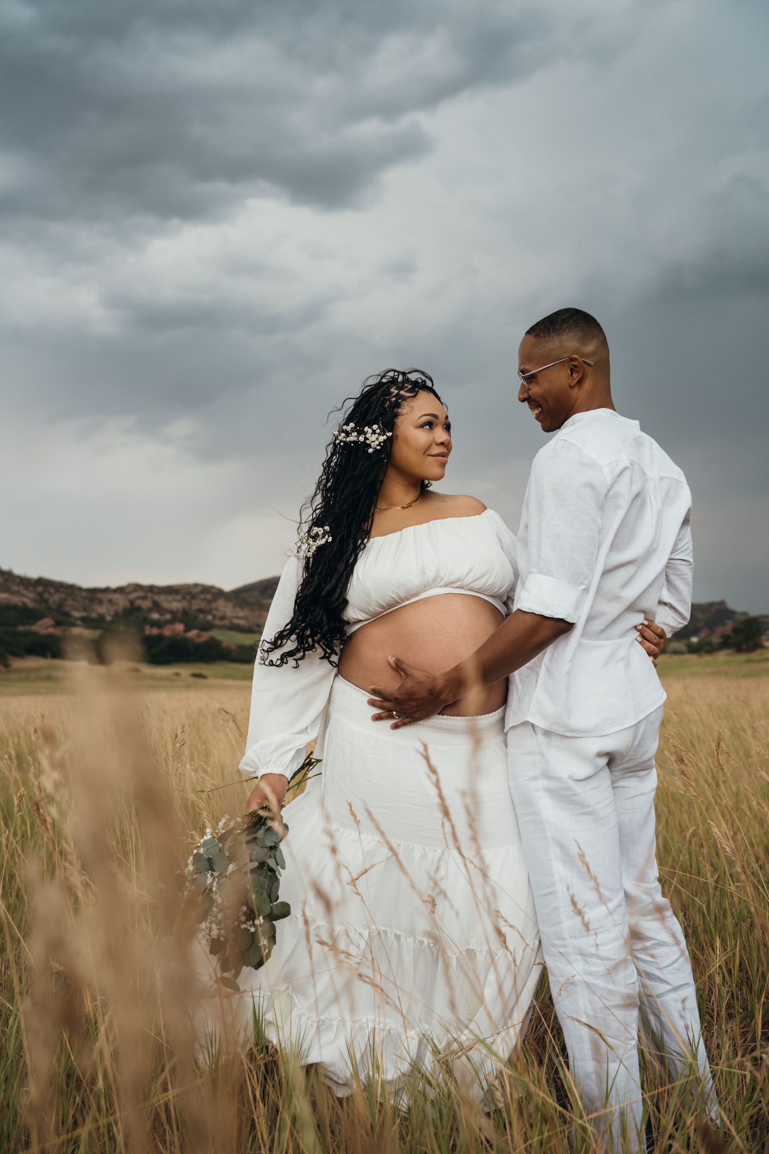 Romantic couple in white outfits embracing in tall grass field under moody cloudy sky in series of connected photos.