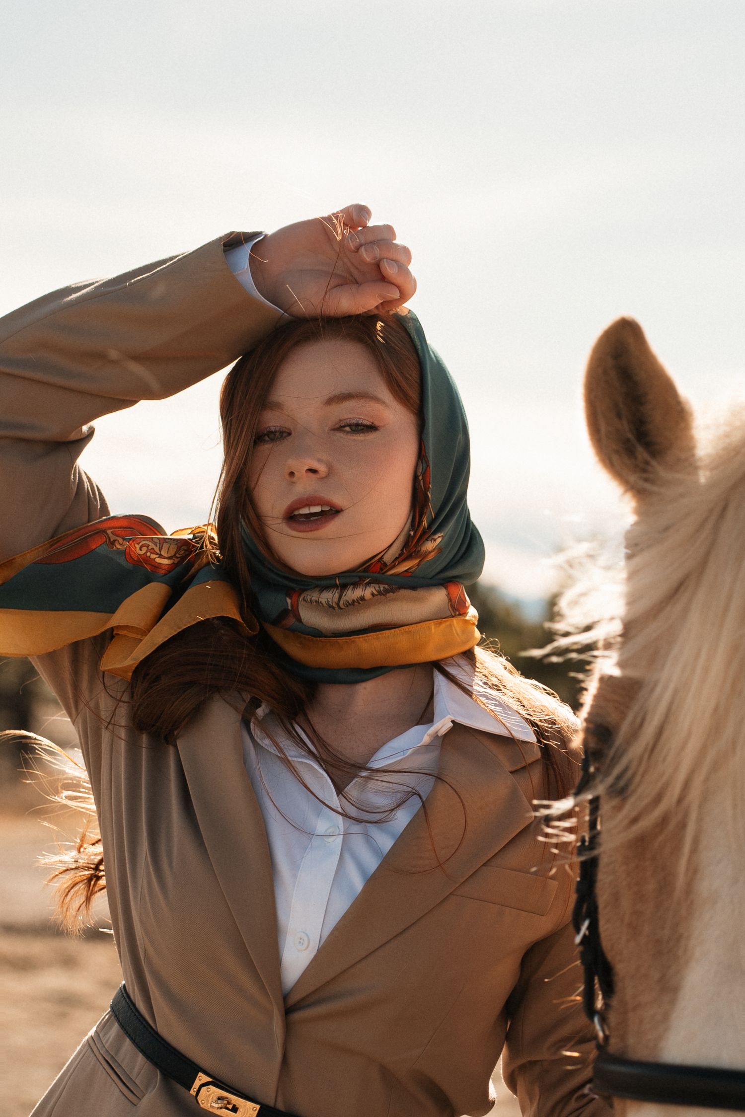 A person in a brown coat and colorful scarf rides horseback during golden hour.