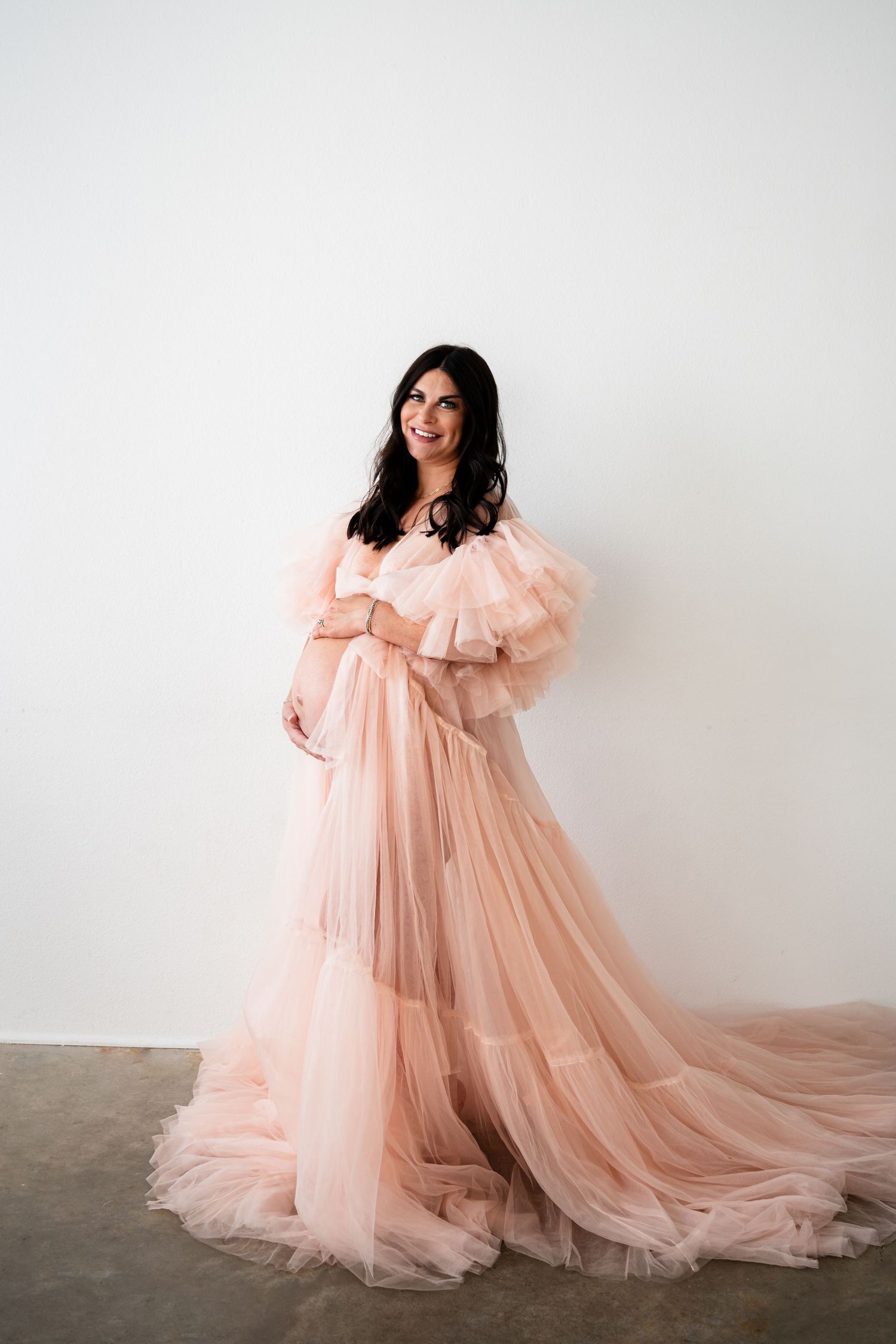 Ethereal maternity portrait in flowing peach tulle gown against white backdrop.