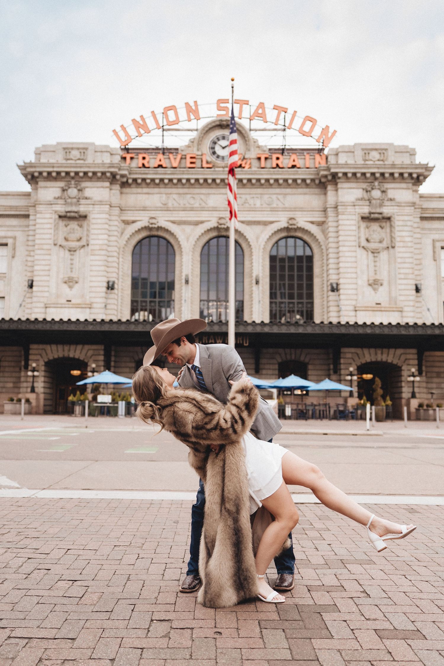 Couple poses for romantic photos in front of historic Union Station building with brick pavement.