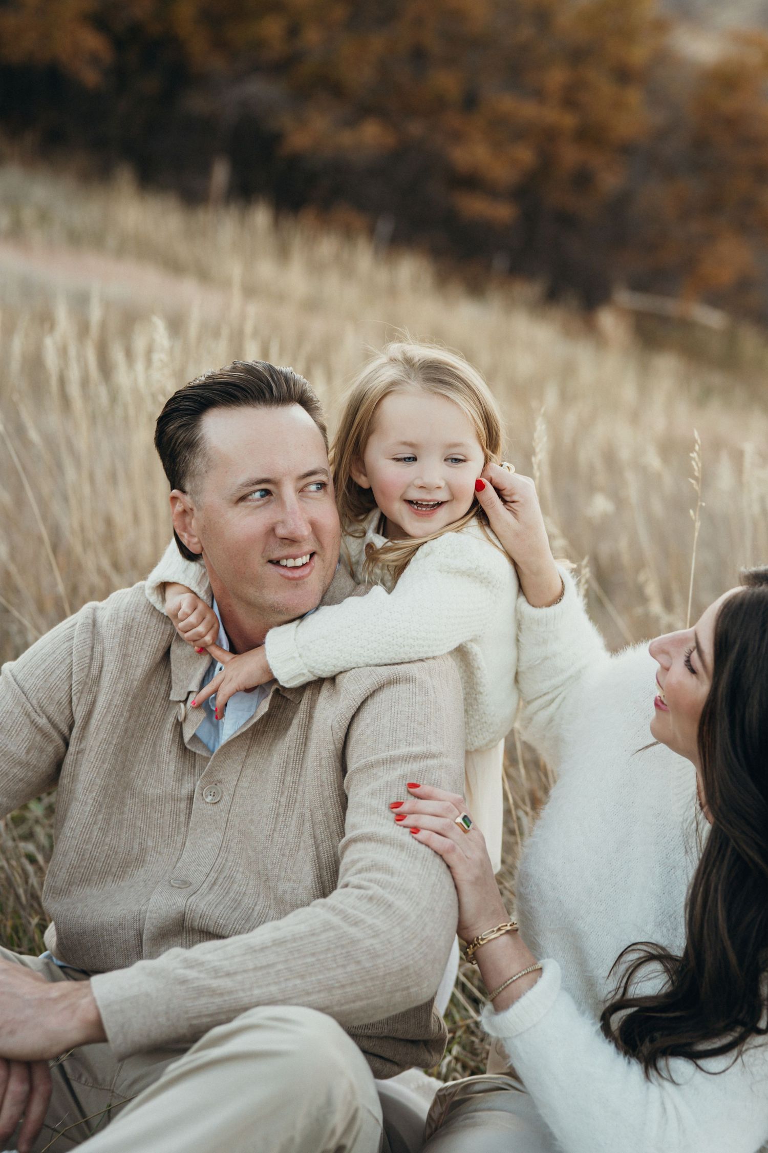 A family shares playful moments together while lying in a field of tall grass during an autumn photoshoot.