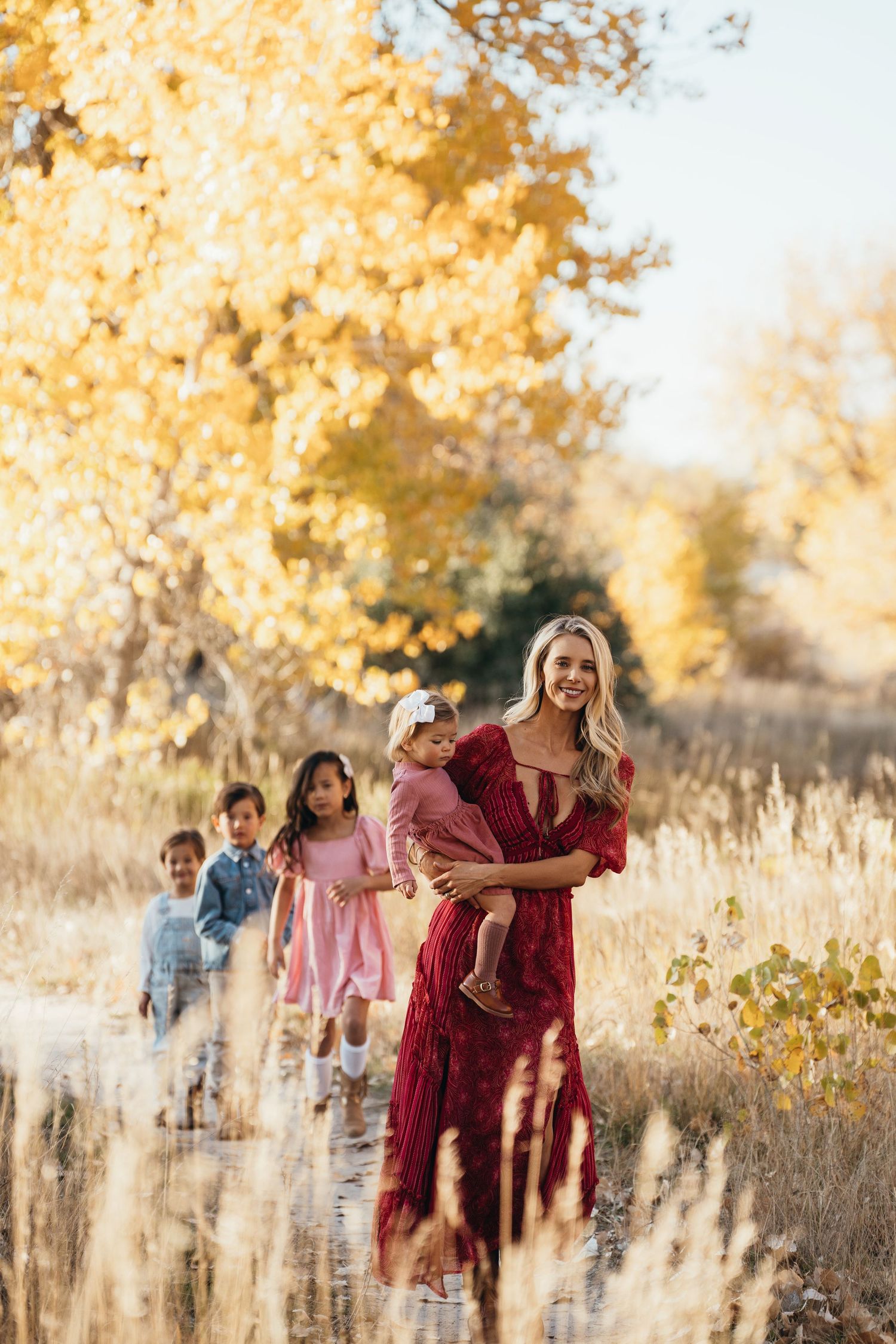 A family walks through a golden autumn field at sunset with tall grass and trees in warm evening light.